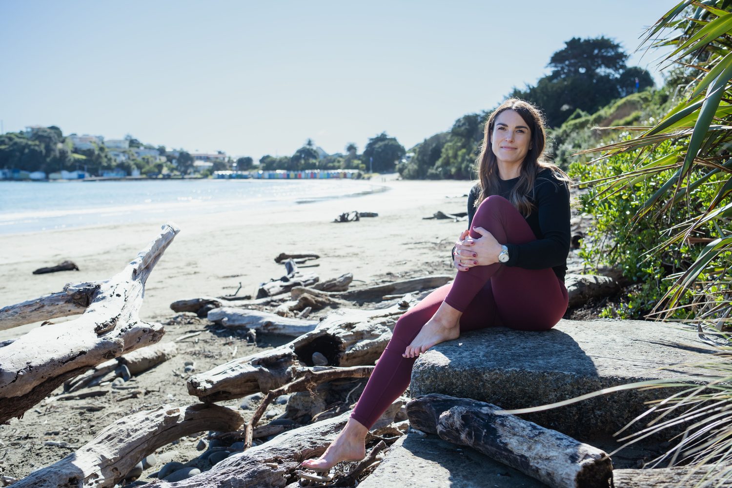 Jess Drayton sitting on driftwood at the water's edge, laughing