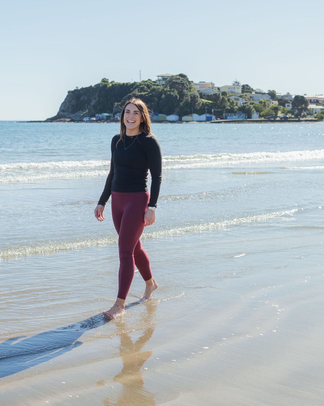 Jess Drayton walking barefoot along the shoreline on a bright morning