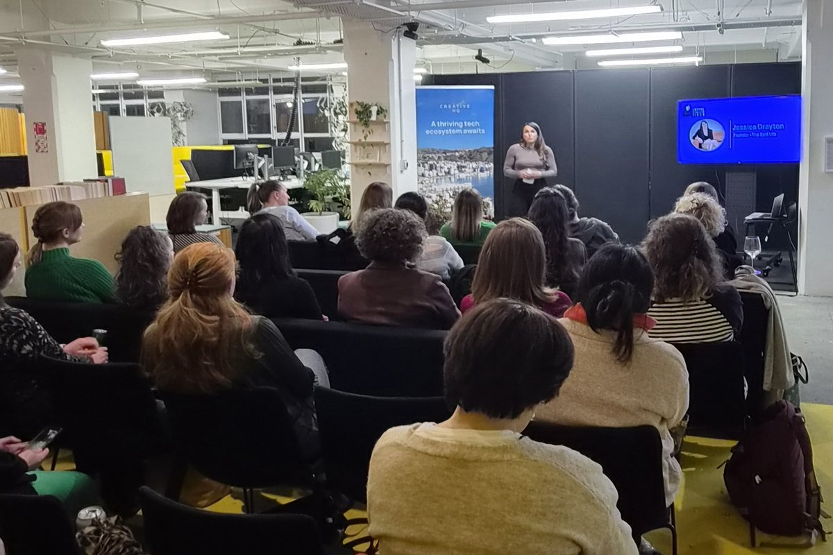 Jess Drayton speaking at the front of a full room, seen from a seat in the audience